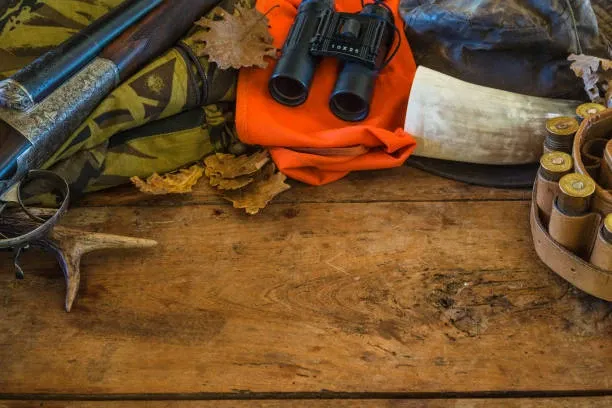 Hunting gear organized on a wood table, including bows, binoculars, and hunting accessories.
