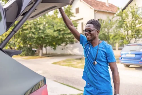 Smiling healthcare professional in scrubs unloading a car.