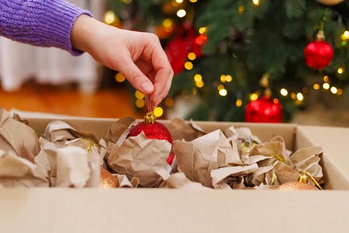 A hand packing a red Christmas ornament in a box filled with paper packaging