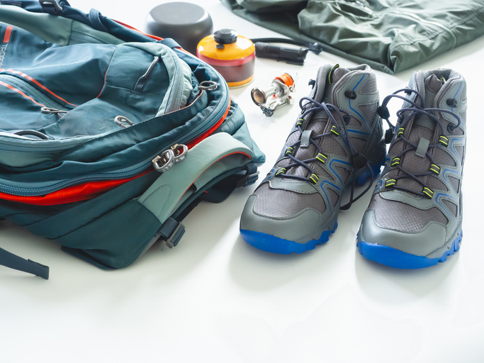 A backpack, hiking boots, and other hiking gear resting on a white surface with a white background.