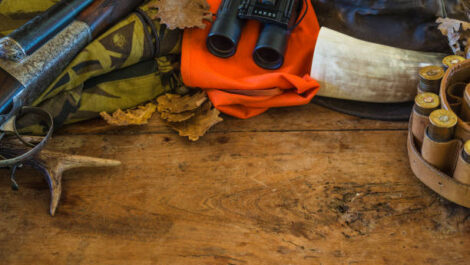 Hunting gear organized on a wood table, including bows, binoculars, and hunting accessories.