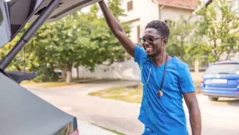 Smiling healthcare professional in scrubs unloading a car.